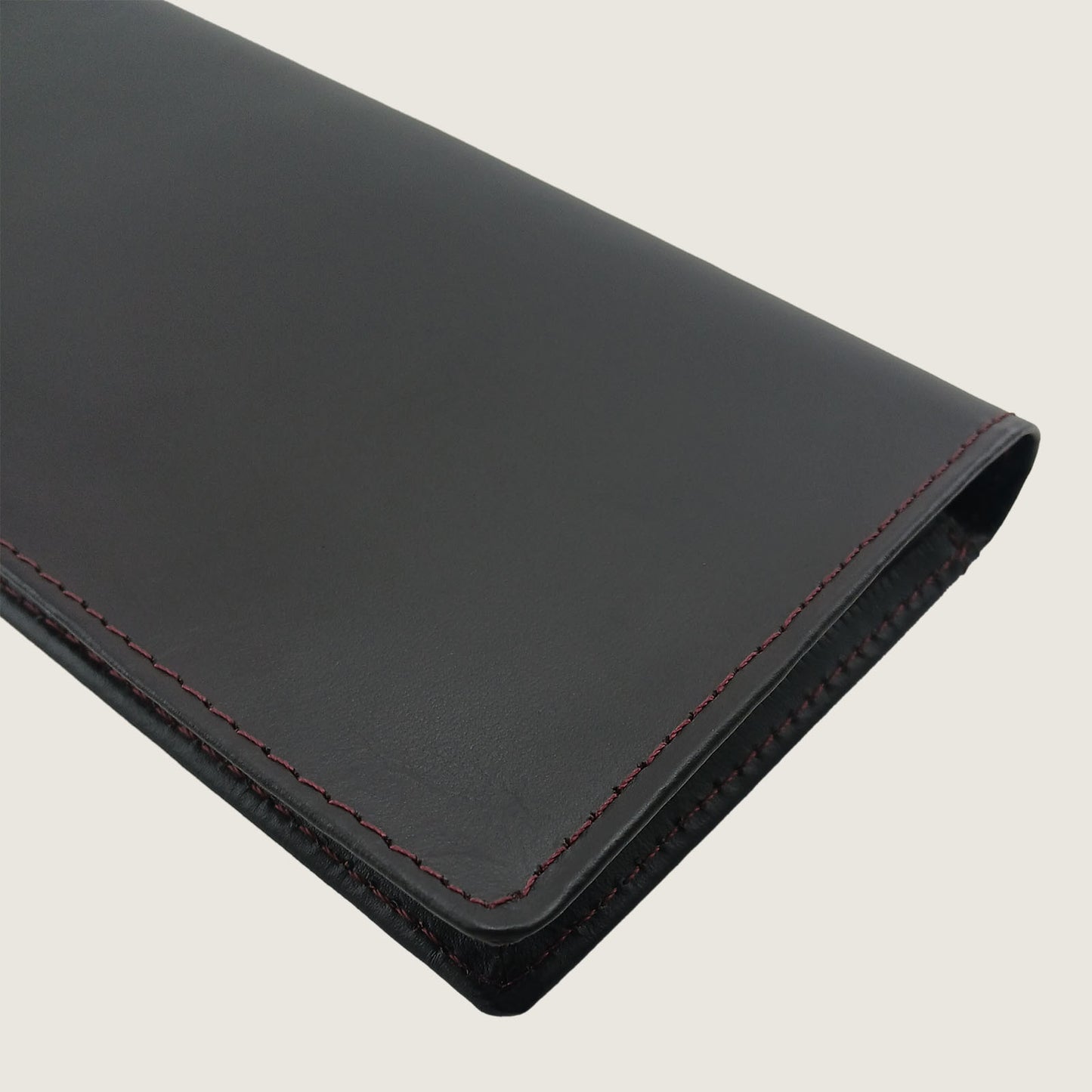 A close-up of a black leather sleeve or folio with red contrast stitching, shown on a light beige background.