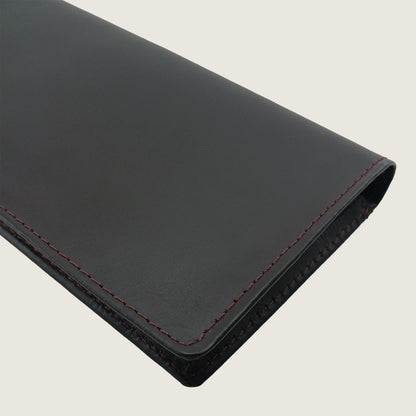 A close-up of a black leather sleeve or folio with red contrast stitching, shown on a light beige background.